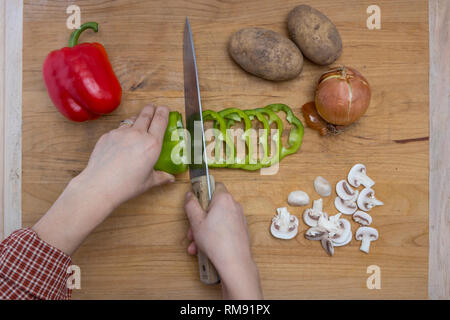 L atto di taglio di un assortimento di verdure su un tagliere. Foto Stock