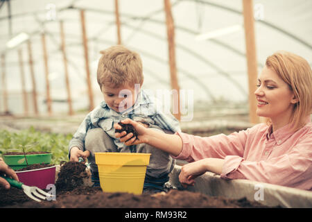 Ragazzino con la madre. la madre e il bambino a lavorare in una moderna serra giardino. La madre e il bambino piantare. felice giorno della madre e un po' Foto Stock