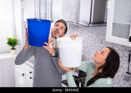 Close-up di un preoccupato coppia giovane la raccolta di perdite di acqua dal soffitto nel secchio blu Foto Stock