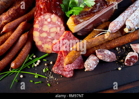 Selezione di essiccato piccante di carne di maiale e manzo salsicce, salami e pancetta o prosciutto cotto con erbe fresche su un tavolo in legno visto da vicino un angolo alto Foto Stock