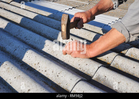 Copritetti installazione tetto in amianto fogli con chiodo e martello nelle sue mani. Coperture in amianto costruzione. Foto Stock