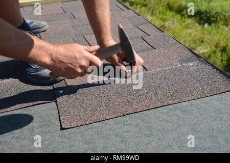 Copritetti Installazione di scandole di asfalto sulla casa costruzione tetto angolo con martello e chiodi. Costruzione di tetti con scandole di asfalto. Foto Stock