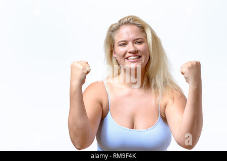 Entusiastico giubilanti giovane donna che mostra la sua beatitudine fustellatura dell'aria con i suoi pugni dopo una vittoria o successo isolato su bianco Foto Stock