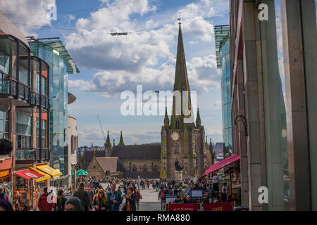 BIRMINGHAM, Regno Unito - Marzo 2018 multirazziale gente camminare lungo la strada molto trafficata in città. Cattedrale con alta torretta e grande orologio in background. Ca Foto Stock