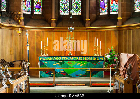 BIRMINGHAM, Regno Unito - Marzo 2018 Coro Area in chiesa per coro e del clero. In vetro colorato e Legno pannello parete come sfondo. Croce celtica e candelabro H Foto Stock