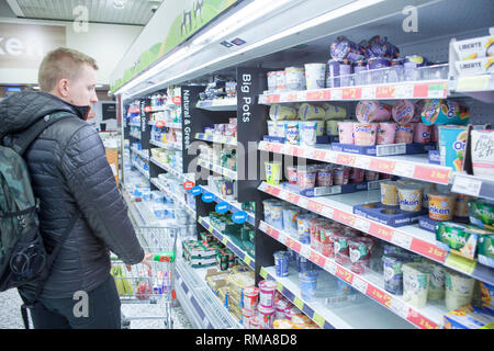 BIRMINGHAM, Regno Unito - Marzo 2018 ASDA uomo in giacca di pelle e zaino è leggere e pensare quello che yogurt per acquistare. Diverso sapore di frutta di nutriente Foto Stock