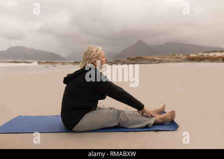 Senior donna stretching su un compagno di yoga sulla spiaggia Foto Stock