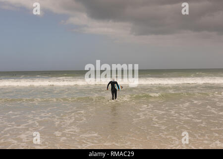 Senior surfista femmina a piedi con la tavola da surf in spiaggia Foto Stock