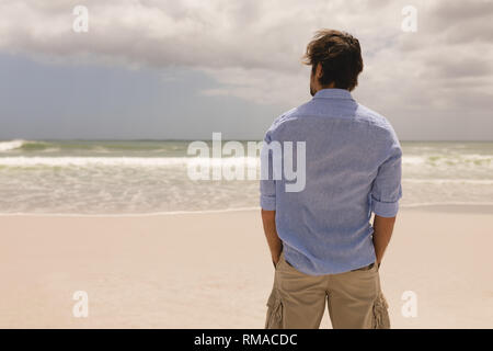 Uomo in piedi con le mani in tasca sulla spiaggia Foto Stock