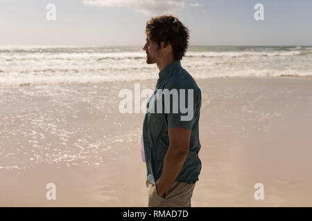 Giovane uomo con la mano in tasca permanente sulla spiaggia Foto Stock