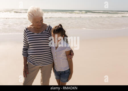 Senior donna e suo nipote con bracci intorno a piedi sulla spiaggia Foto Stock
