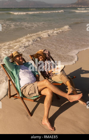 Coppia senior avendo divertimento mentre vi rilassate sulla sedia a sdraio in spiaggia Foto Stock
