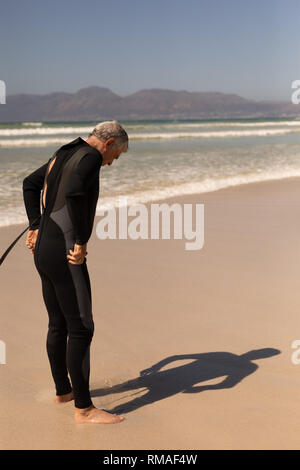 Vista laterale del maschio senior surfer indossando muta sulla spiaggia Foto Stock