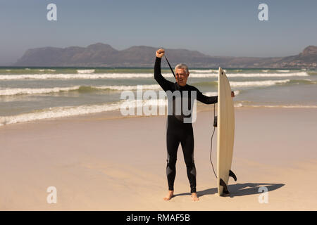 Vista laterale del senior surfista maschio in piedi con la tavola da surf in spiaggia Foto Stock