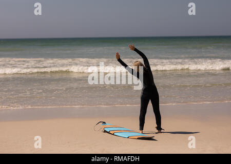 Vista posteriore femmina senior del surfista con la tavola da surf che esercitano sulla spiaggia Foto Stock