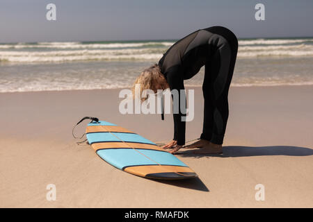 Vista laterale della femmina senior del surfista con la tavola da surf che esercitano sulla spiaggia Foto Stock