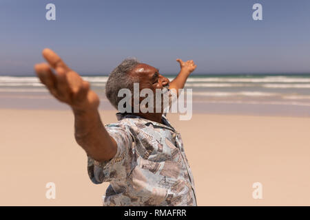 Senior uomo nero con le braccia aperte in piedi sulla spiaggia Foto Stock