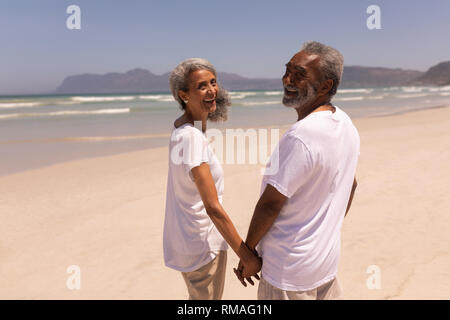 Felice coppia senior tenendo le mani e guardando la telecamera sulla spiaggia Foto Stock