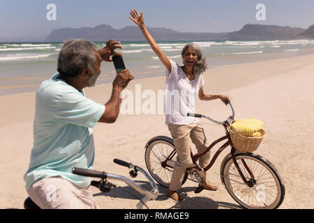 Senior uomo facendo clic su foto di donna senior con telefono cellulare sulla spiaggia Foto Stock