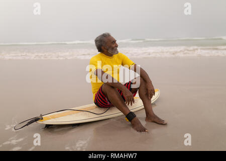 Senior surfista maschile seduto sulla tavola da surf in spiaggia Foto Stock