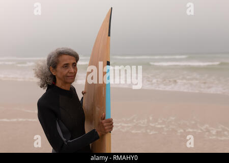 Femmina Senior del surfista con la tavola da surf in piedi sulla spiaggia Foto Stock