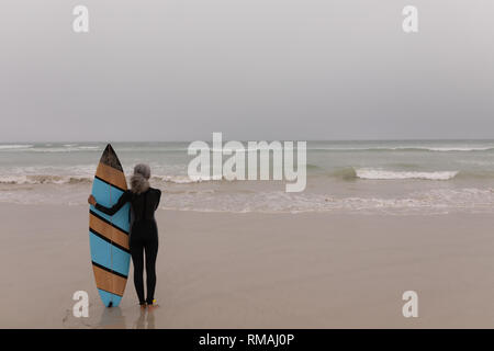 Femmina Senior del surfista con la tavola da surf in piedi sulla spiaggia Foto Stock