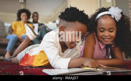 Carino americano africano i gemelli sdraiato sul pavimento e la lettura di un libro delle fiabe Foto Stock