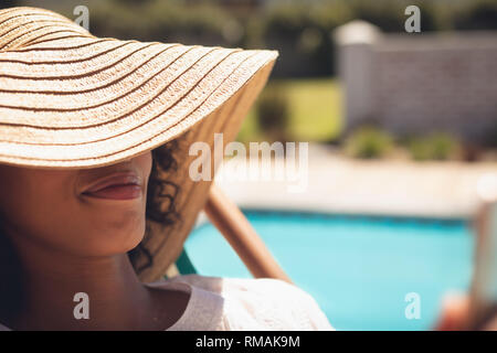 African American donna con cappello rilassandovi sulle sdraio nel suo cortile Foto Stock