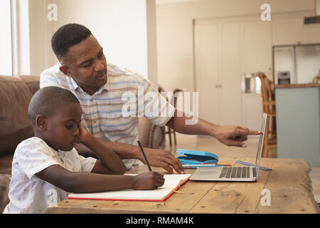 African American padre aiutando il suo figlio con i compiti di un portatile a tavola Foto Stock