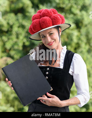 Un ritratto di una bella cameriera tedesca tenendo un menu in abbigliamento tradizionale indossando un bollenhut. Foto Stock