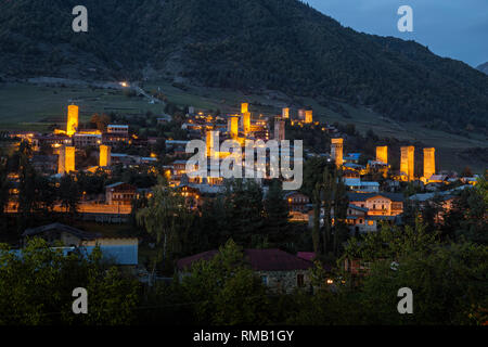 Mestia al crepuscolo, illuminato Svan torri sullo sfondo di un pendio montano, Svaneti superiore, Georgia Foto Stock