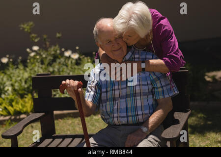 Senior donna abbracciando e baciando senior l uomo nel giardino Foto Stock