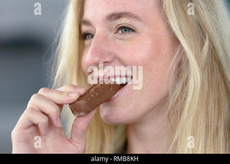 Ritratto di giovane Allegra donna bionda mangiando cioccolato, vicino. Foto Stock