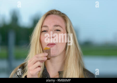 Ritratto di giovane sorridente donna bionda mangiare il cioccolato Foto Stock