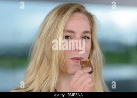 Ritratto di giovane sorridente donna bionda mangiare il cioccolato Foto Stock