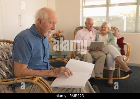 Cieco uomo senior la lettura di un libro in braille mentre la coppia senior con tavoletta digitale presso la casa di cura Foto Stock