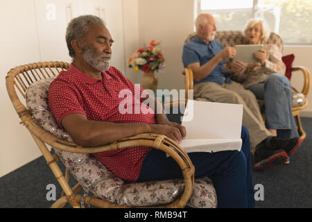 Cieco uomo senior la lettura di un libro in braille mentre la coppia senior con tavoletta digitale presso la casa di cura Foto Stock