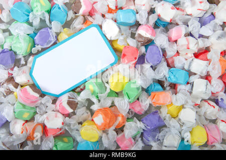 Sfondo di acqua salata taffy in vari sapori e colori avvolto in bianco carta trasparente, scheda vuota sulla parte superiore. Acqua salata taffy è venduta su Foto Stock