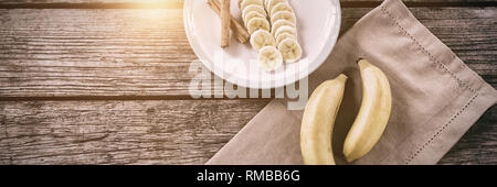 Banana e fette di banana con la stecca di cannella in piastra sul tavolo di legno Foto Stock