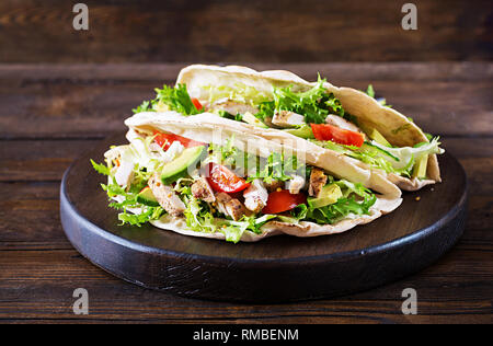 Panini di pita con pollo grigliato carne, avocado, pomodori, cetrioli e lattuga servita su sfondo di legno. Close up. Un sano fast food conce Foto Stock