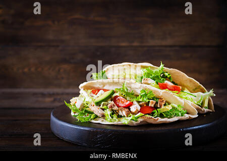 Panini di pita con pollo grigliato carne, avocado, pomodori, cetrioli e lattuga servita su sfondo di legno. Close up. Un sano fast food conce Foto Stock