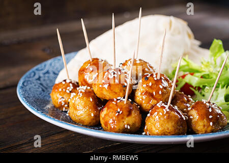 Le polpette di carne in agrodolce smalto su una piastra con pane pita e verdure in uno stile Marocchino su un tavolo di legno. Le tapas. Cibo di tendenza. Foto Stock