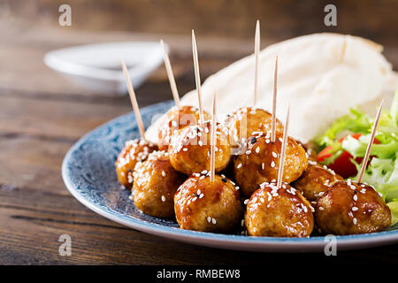 Le polpette di carne in agrodolce smalto su una piastra con pane pita e verdure in uno stile Marocchino su un tavolo di legno. Le tapas. Cibo di tendenza. Foto Stock