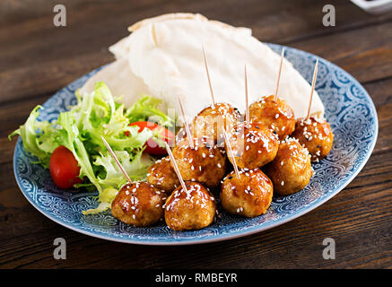 Le polpette di carne in agrodolce smalto su una piastra con pane pita e verdure in uno stile Marocchino su un tavolo di legno. Le tapas. Cibo di tendenza. Foto Stock