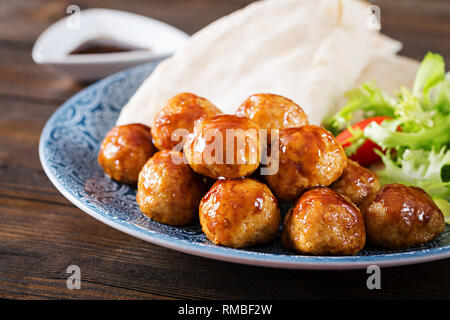 Le polpette di carne in agrodolce smalto su una piastra con pane pita e verdure in uno stile Marocchino su un tavolo di legno. Le tapas. Cibo di tendenza. Foto Stock