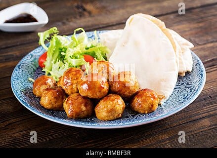 Le polpette di carne in agrodolce smalto su una piastra con pane pita e verdure in uno stile Marocchino su un tavolo di legno. Le tapas. Cibo di tendenza. Foto Stock