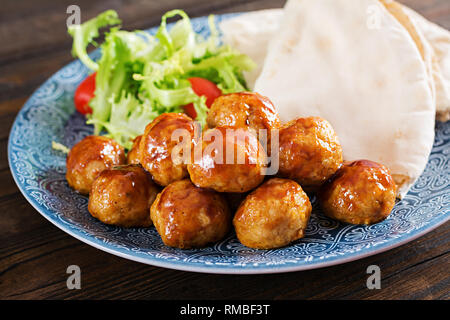 Le polpette di carne in agrodolce smalto su una piastra con pane pita e verdure in uno stile Marocchino su un tavolo di legno. Le tapas. Cibo di tendenza. Foto Stock
