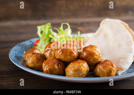Le polpette di carne in agrodolce smalto su una piastra con pane pita e verdure in uno stile Marocchino su un tavolo di legno. Le tapas. Cibo di tendenza. Foto Stock