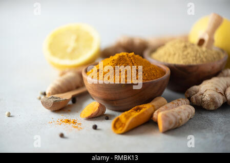 Ingredienti per la calda bevanda ayurvedica. La curcuma in polvere, curcuma radice, la cannella, lo zenzero, limone su sfondo grigio. Spazio di copia, quadrato raccolto. Spezie per Foto Stock