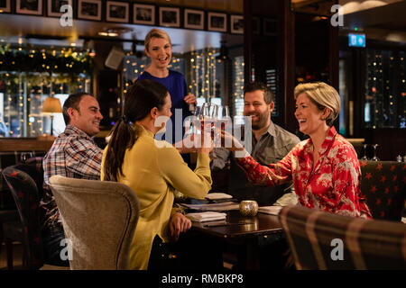 Due coppie mature facendo un brindisi celebrativo con un bicchiere di vino rosato mentre è seduto in un ristorante. Foto Stock